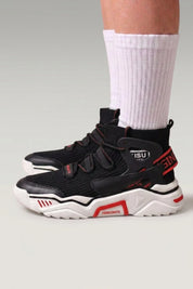 High-Top-Sneaker 'Echizen' in Schwarz — zwei breite Riemen, gepolsterter Schaft, rote Details, am Fuß mit weißen Socken vor grauem Studiohintergrund